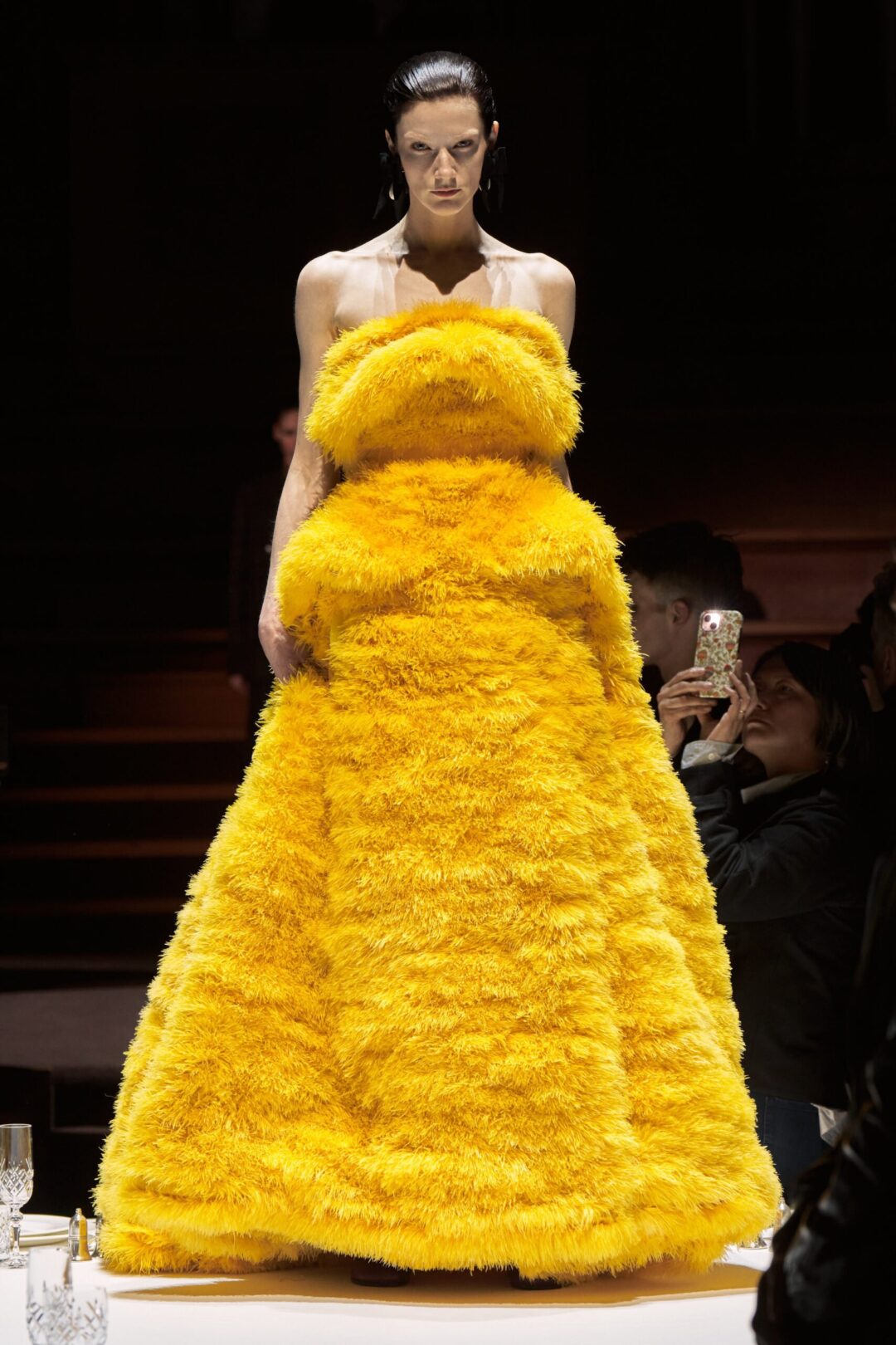 A model posing on the catwalk, wearing a yellow dress made of fur.